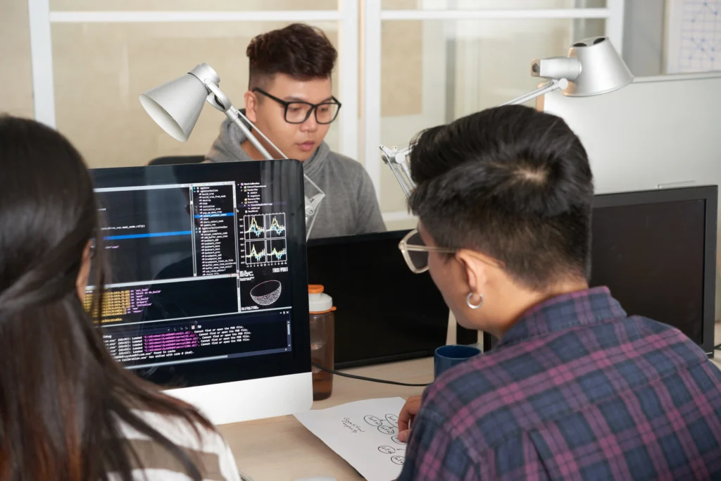 Developers collaborating at a computer reviewing code and application architecture for web development frameworks