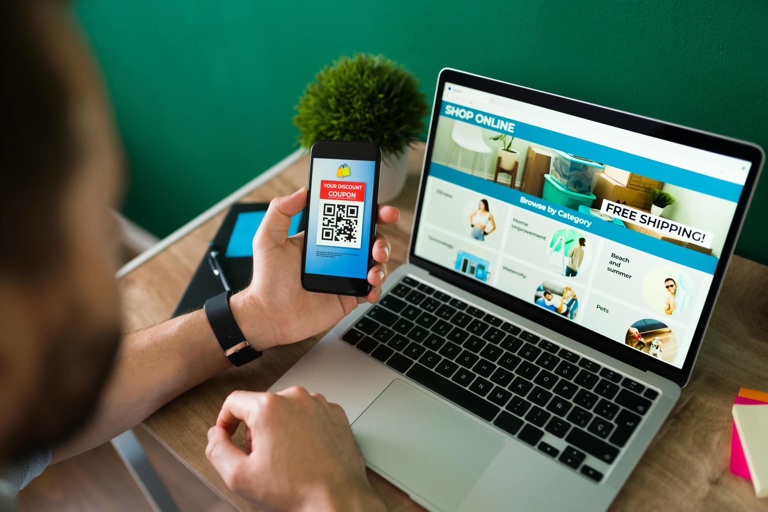 Person browsing an online store on a laptop while viewing a digital discount coupon on a smartphone, highlighting the importance of modern e-commerce web design in 2026